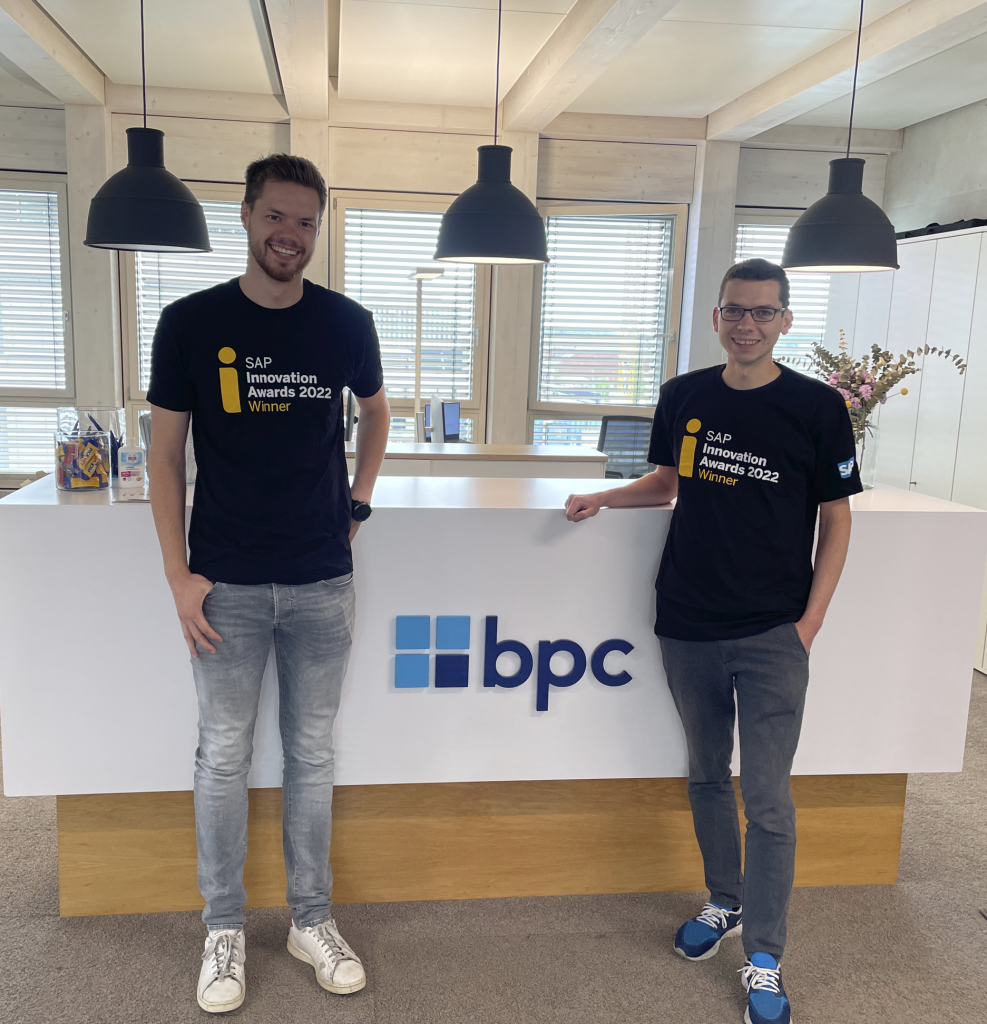 Two men standing at BPC desk smiling with SAP Award tee shirts